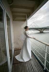 美丽的年轻新娘在阳台上摆姿势看着河流图片