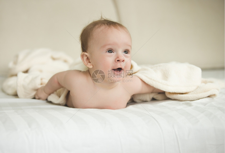 令人惊讶的婴儿男孩有趣肖像躺在床上的毯子下躺在图片