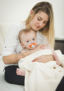 年轻有爱心的母亲坐在床上手握着婴儿的触摸画像背景图片