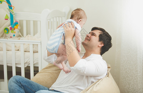 快乐的年轻父亲肖像坐在袋子椅上和他6个月的儿子玩耍图片