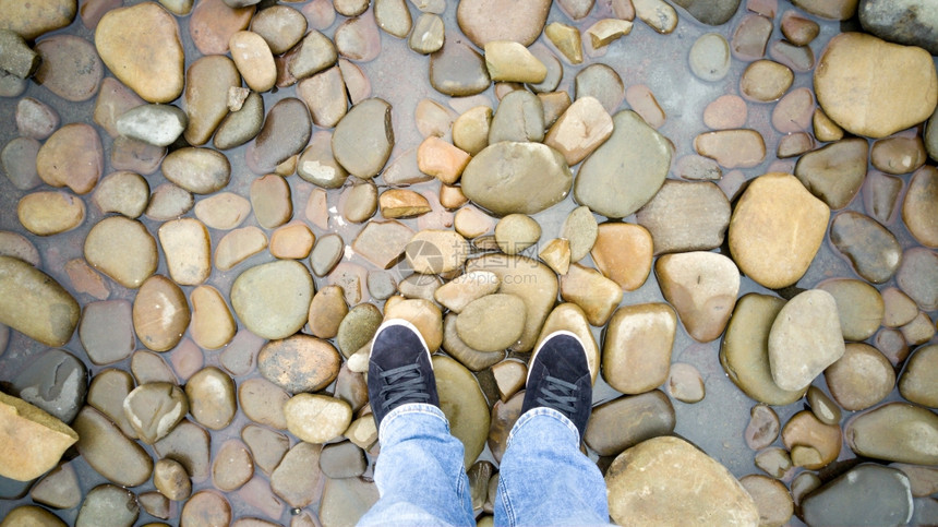 穿着运动鞋的男脚站在海中的石块上图片