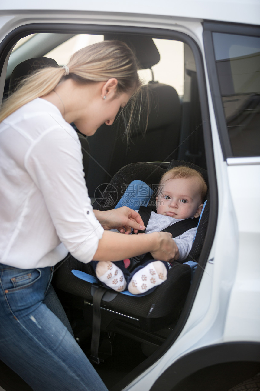 年轻母亲把婴儿放在汽车安全座椅上图片