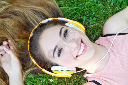 女孩在夏天草地上听音乐着用耳机播放的音乐图片