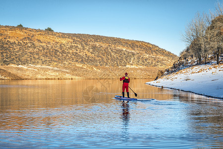 穿红色干衣的男球正在科罗拉多山湖冬季风景中划踏板图片