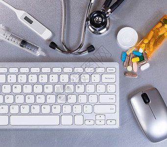 配有计算机键盘听诊器温度计药品老鼠和注射器的医生桌图片