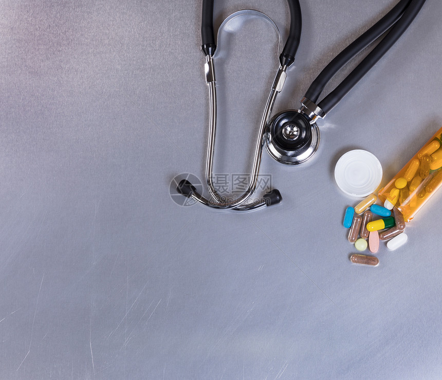不锈钢板上的医学听诊器和药丸的俯视图片