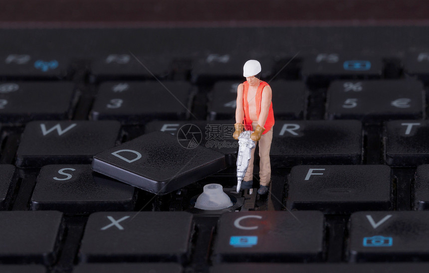 在计算机键盘上操作钻孔的微型工人图片