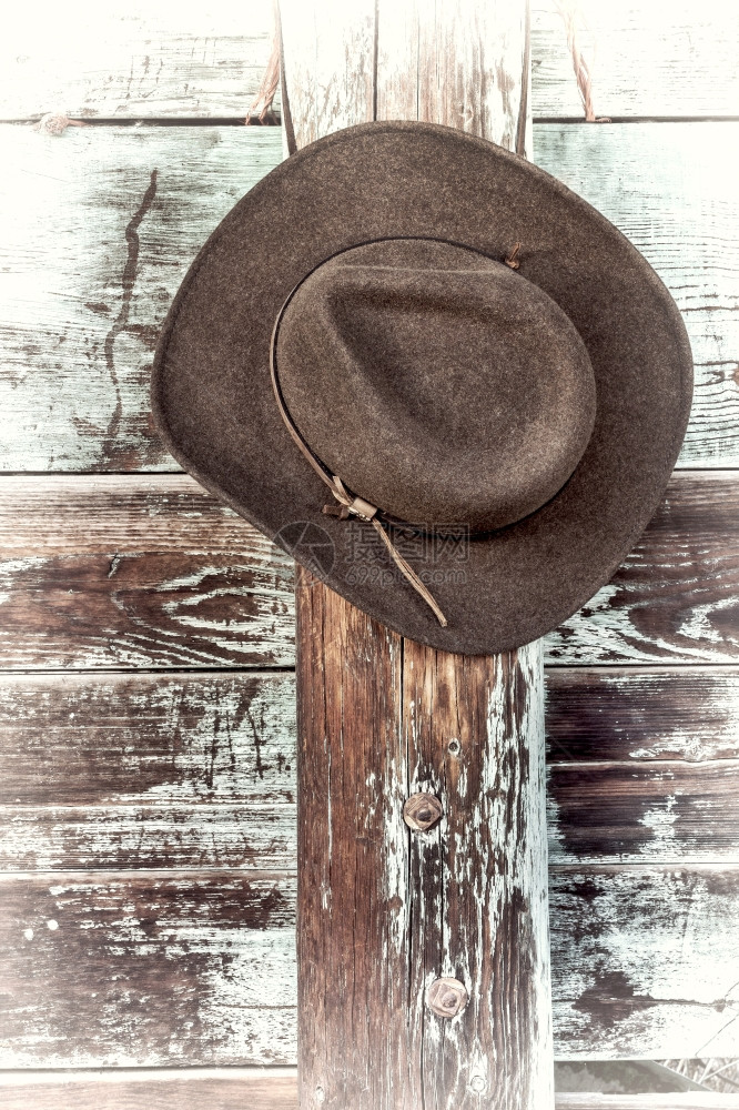 棕色羊毛感觉牛仔帽皮革头带挂在风湿的木椰子栅栏上旧手加色工图片