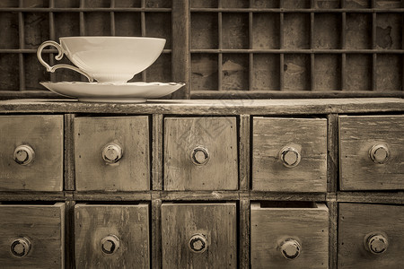 古典茶杯在生锈的药用抽屉柜顶上黑白的金背景图片