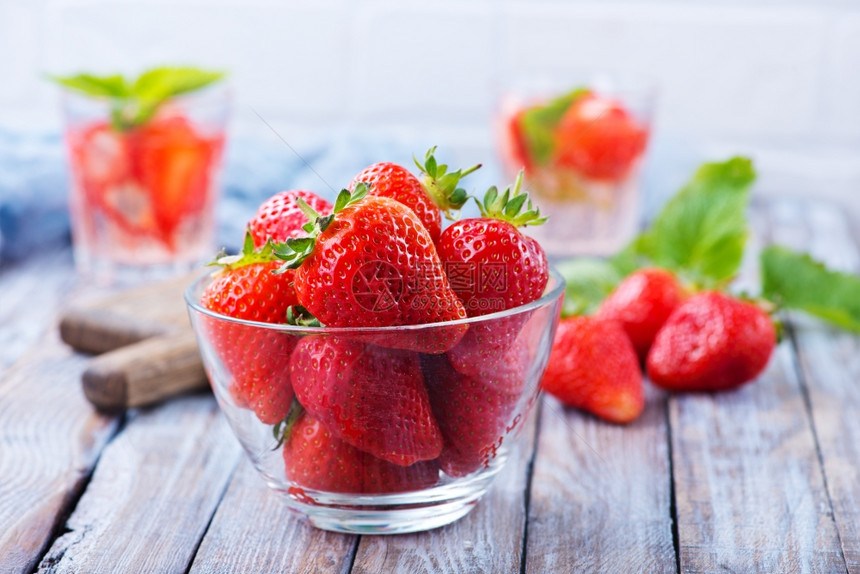 新鲜草莓在碗里和桌子上图片