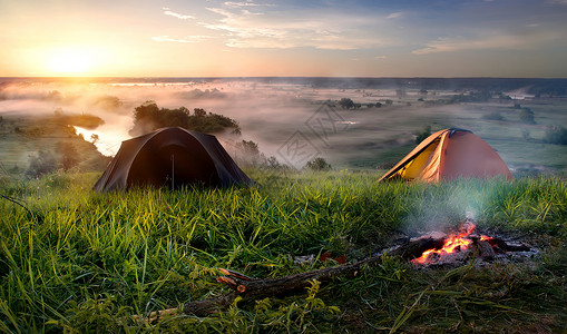 日出时在河附近草原的帐篷和营火高清图片