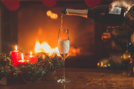 手把香槟倒在玻璃杯里圣诞树和烧火的壁炉图片