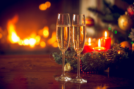 美丽的圣诞背景有两个香槟长笛燃烧壁炉和蜡烛花圈图片