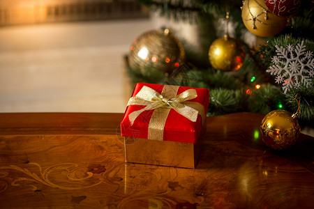 圣诞背景在燃烧的壁炉和圣诞树前面的木桌上装着红色礼品盒图片