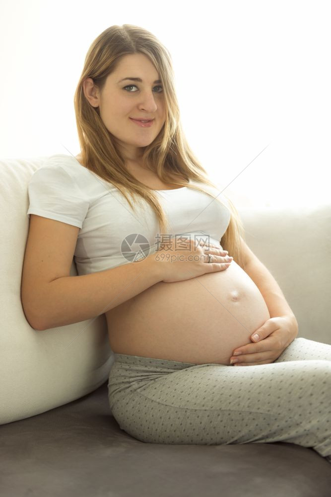 美丽的孕妇在沙发上放松手在肚子上握图片