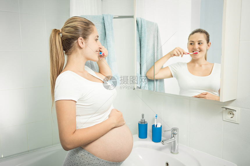 美丽的年轻女子在浴室照镜刷牙的肖像图片