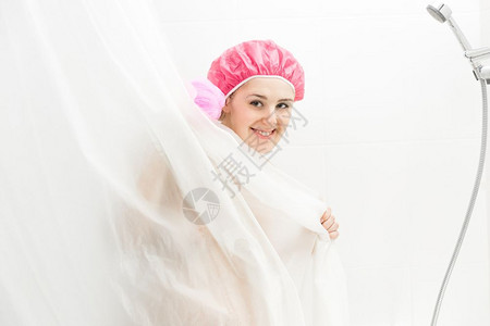 穿着浴帽洗澡和躲在窗帘后面的可爱笑女人肖像高清图片