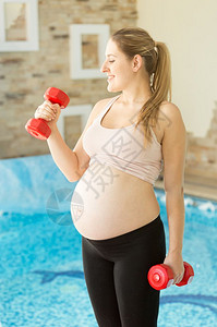 微笑的孕妇在健身房装着哑铃的模样图片