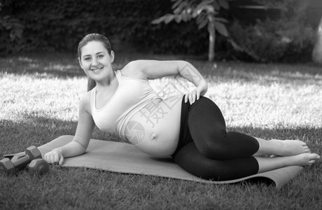 孕妇做哑铃运动年轻孕妇在做瑜伽前公园草地上伸展的黑白画面背景
