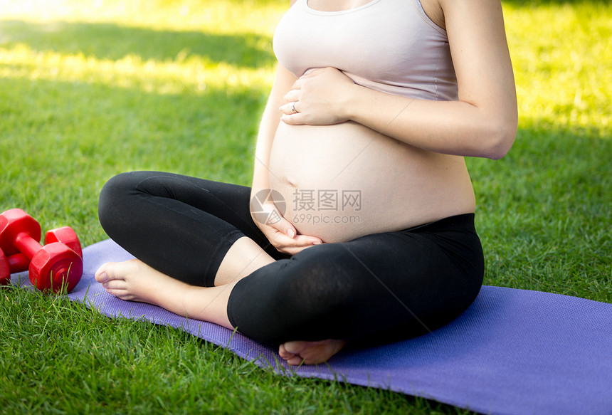 坐在公园草地上触摸大肚子的活跃孕妇图片