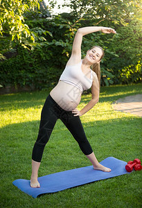 草坪瑜伽美丽的年轻孕妇在公园绿草地上运动背景