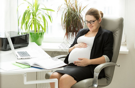 快乐的怀孕女商人在办公室上当主席图片