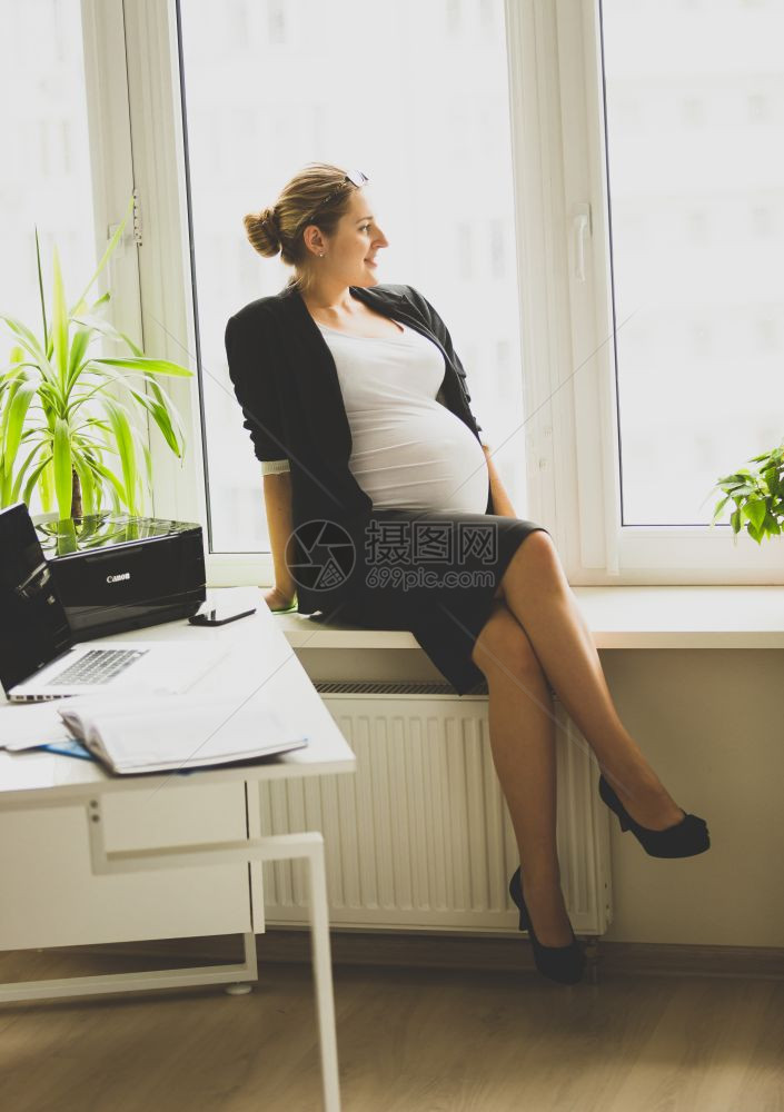 坐在窗台上和电话接听的年轻怀孕女商人图片