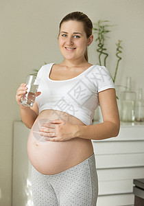 美丽的孕妇拿着杯水看肚子图片