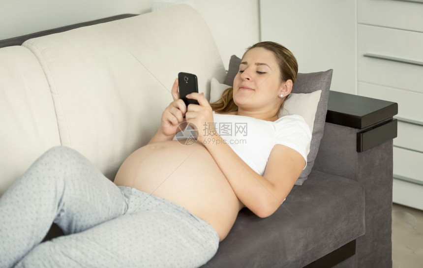 躺在沙发上并使用智能手机的年轻孕妇图片