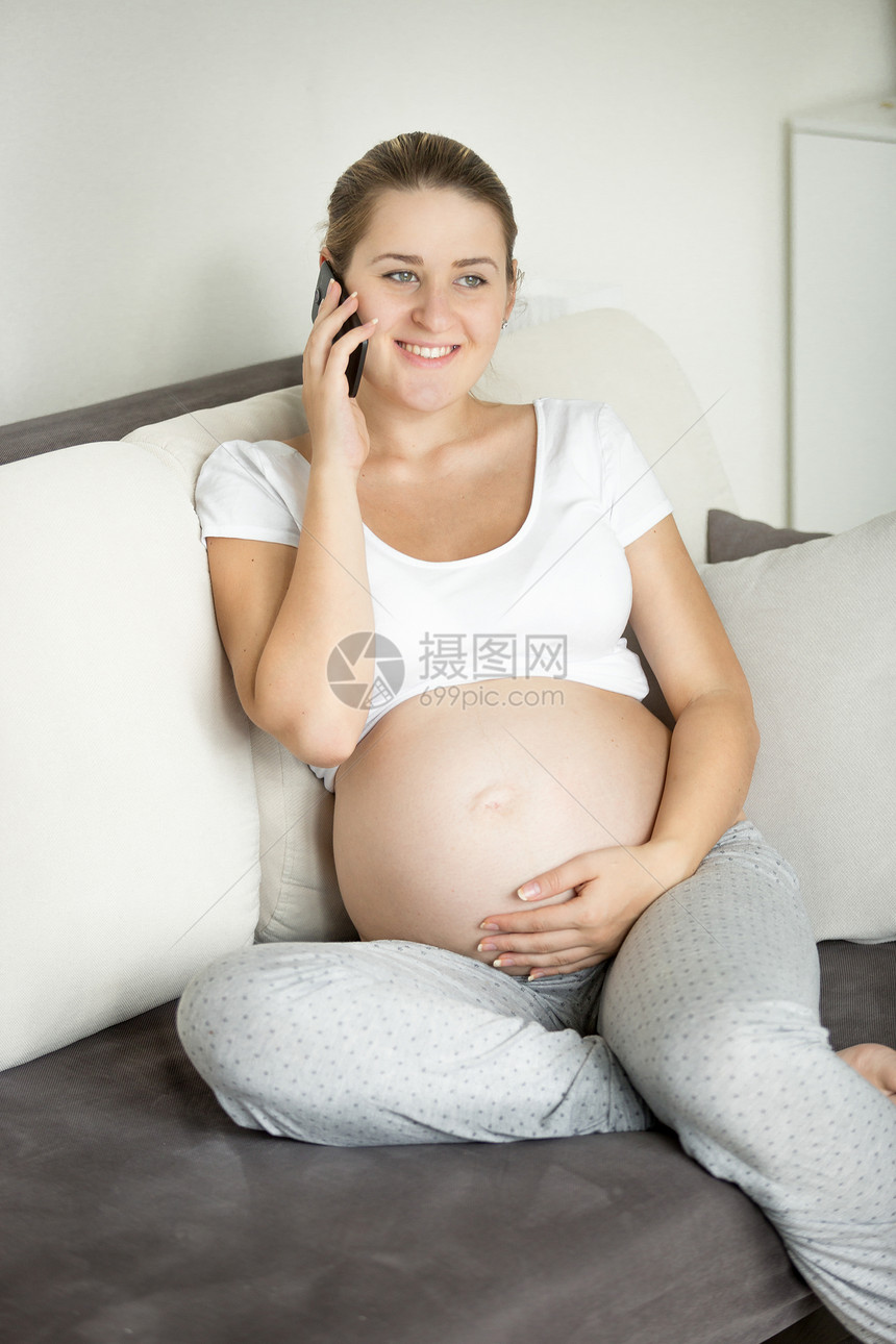美丽的笑着孕妇打电话在沙发上聊天图片