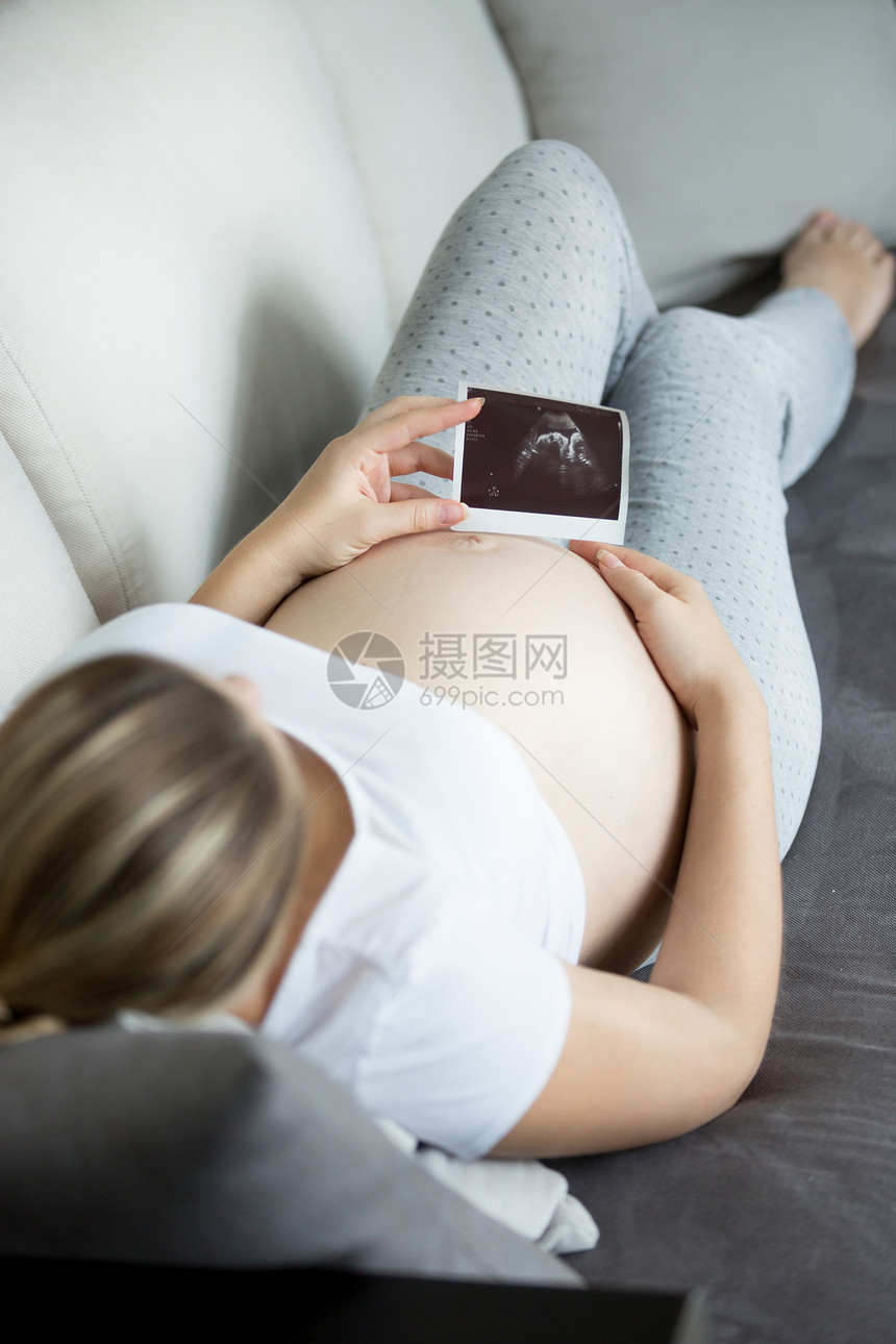 年轻孕妇在沙发上放松和观看超声波婴儿扫描的近照图片