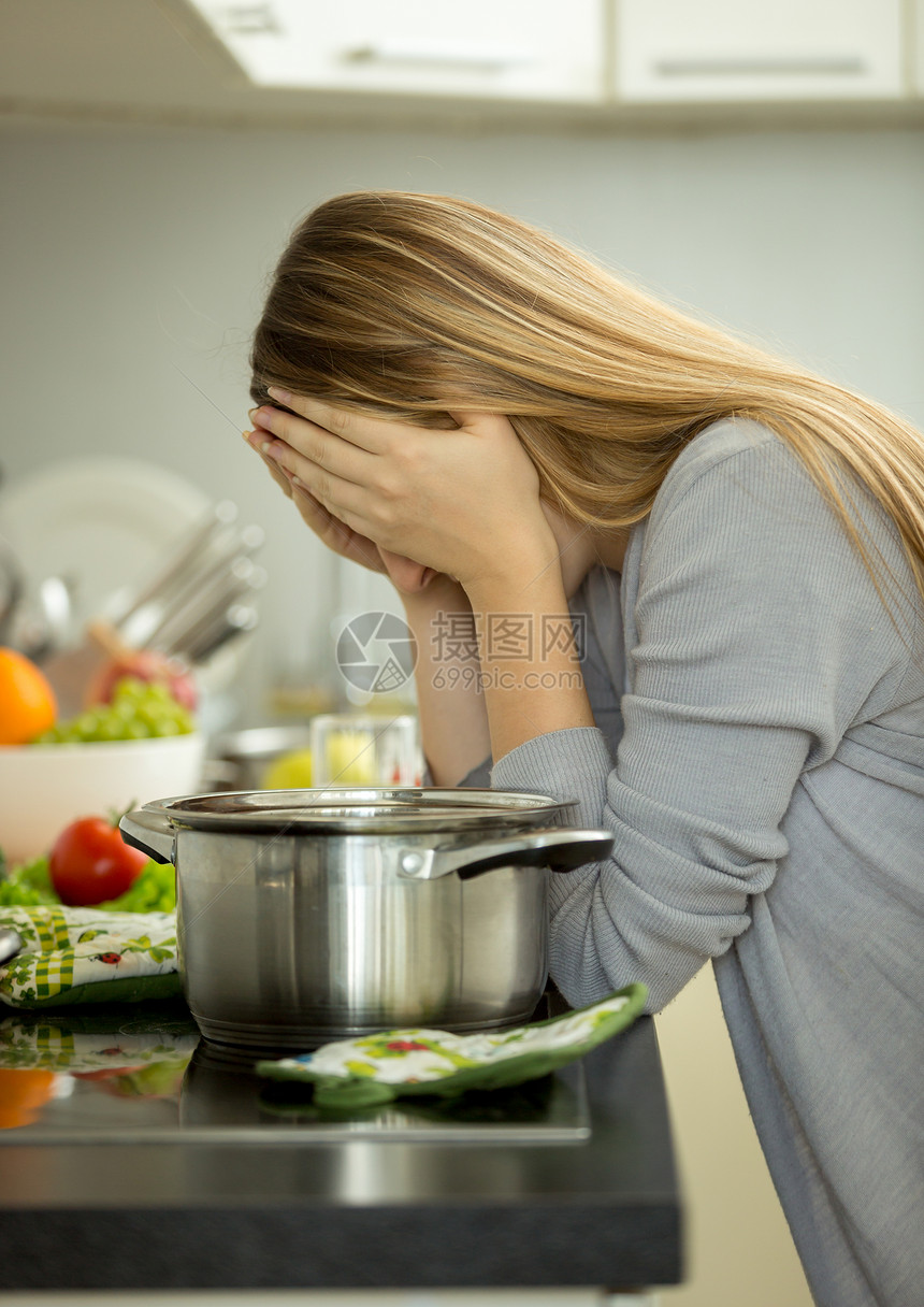 精疲力尽的年轻家庭主妇肖像在煮汤时厨房上摆姿势图片