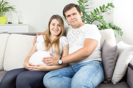 在客厅沙发上坐等待婴儿的快乐年轻夫妇图片