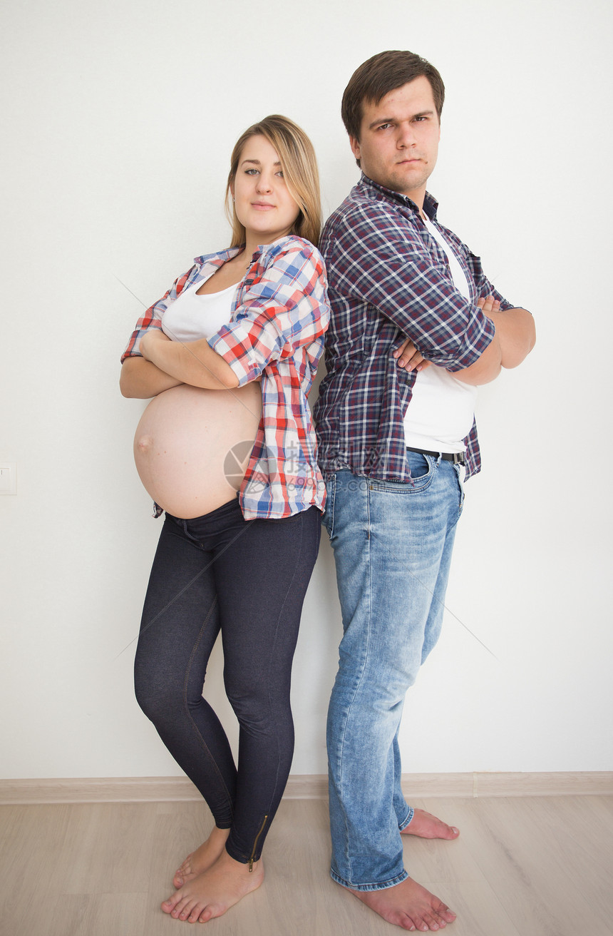 在空房间里靠白墙上的年轻怀孕夫妇图片
