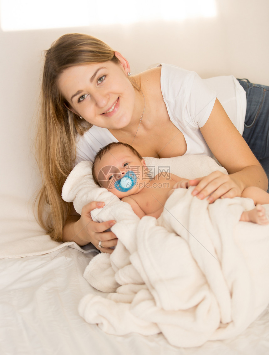 带着新生婴儿躺在床上的快乐笑女人肖像图片