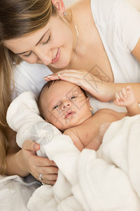抱着新生婴儿躺在床上的年轻有爱护母亲的近身肖像图片