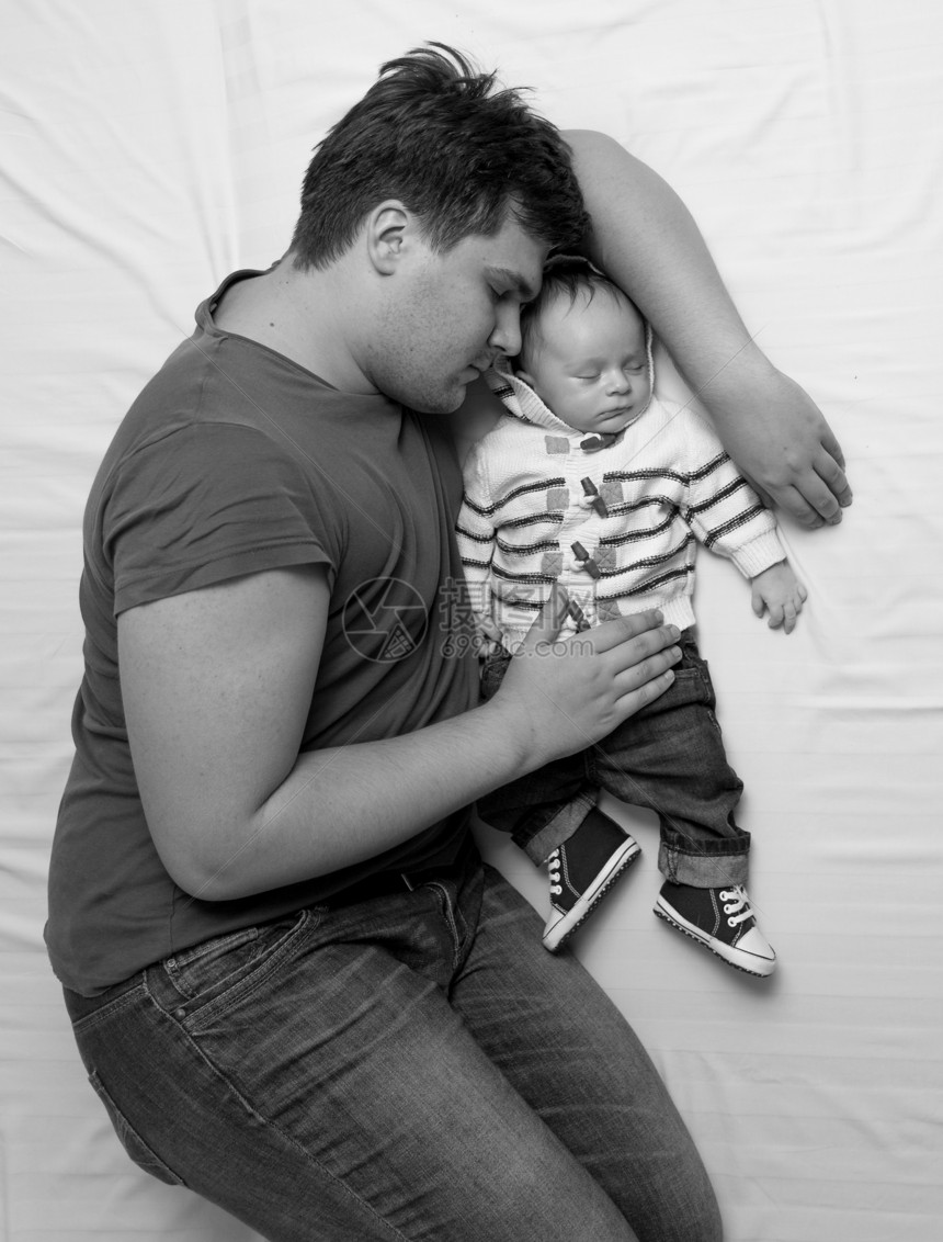 年轻父亲与新生儿男孩在床上睡觉的黑白画像图片