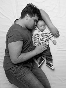 年轻父亲与新生儿男孩在床上睡觉的黑白画像图片