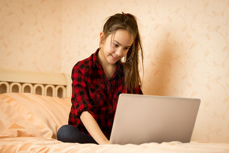 用笔记本电脑坐在卧室床上的年轻女孩图片