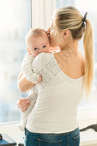 美丽的母亲在窗边拥抱她三个月大的婴儿男孩图片