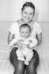 年轻笑的母亲与三个月大的婴儿坐在一起黑人和白色肖像图片