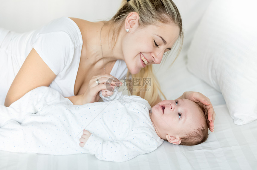 3个月大的婴儿男孩躺在床上年轻的微笑母亲图片