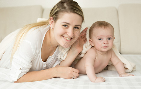 快乐笑的妈和婴儿在床上盖毯子图片