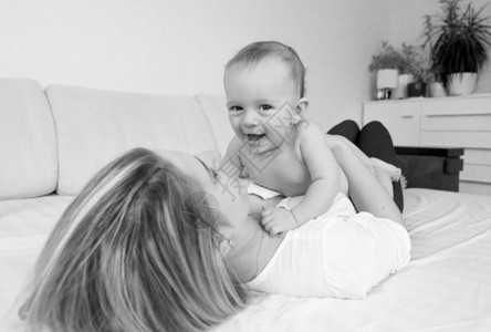 年轻微笑的母亲躺在床上和她6个月的儿子玩耍图片