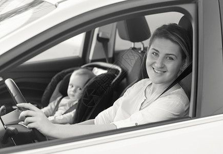 年轻母亲驾驶汽车时婴儿坐在前座的年轻母亲黑白画像背景图片