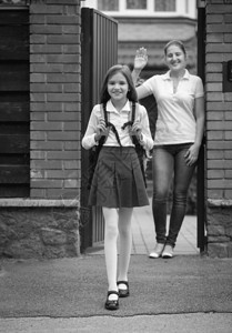 黑色和白的画面美丽微笑女孩在学生面前站在母亲向她挥手图片