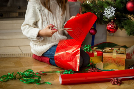 女孩坐在圣诞树和切割包装纸下的照片图片