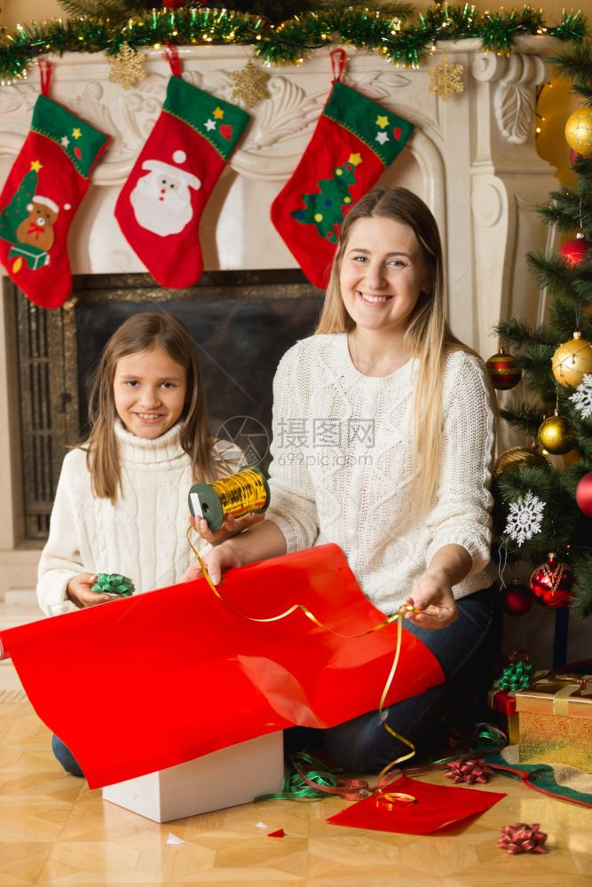 快乐的女孩和母亲坐在壁炉边包着圣诞礼物图片