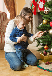 母亲和十个月大的婴儿男孩在家里装饰圣诞树图片