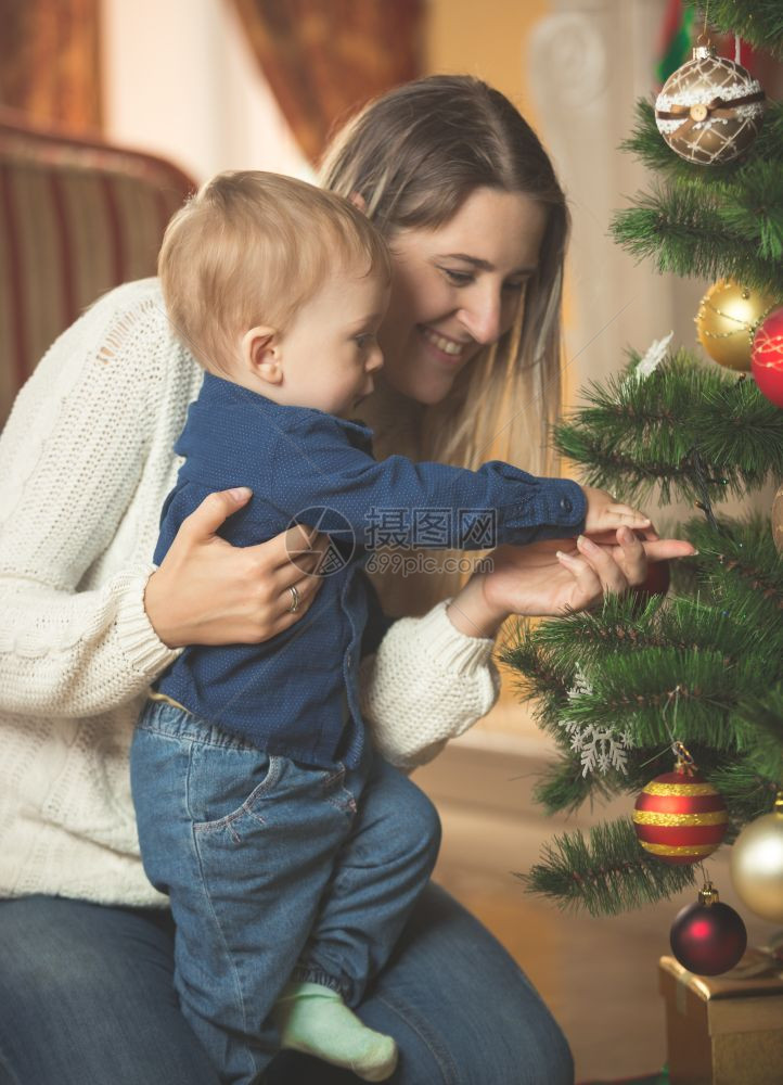 微笑的女人装饰圣诞树与她的10个月大儿子图片